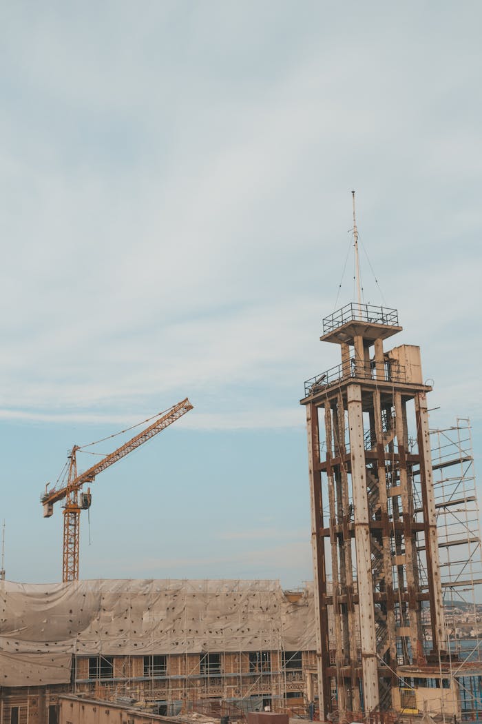 View of a modern urban construction site featuring a crane and a tall tower under blue skies.